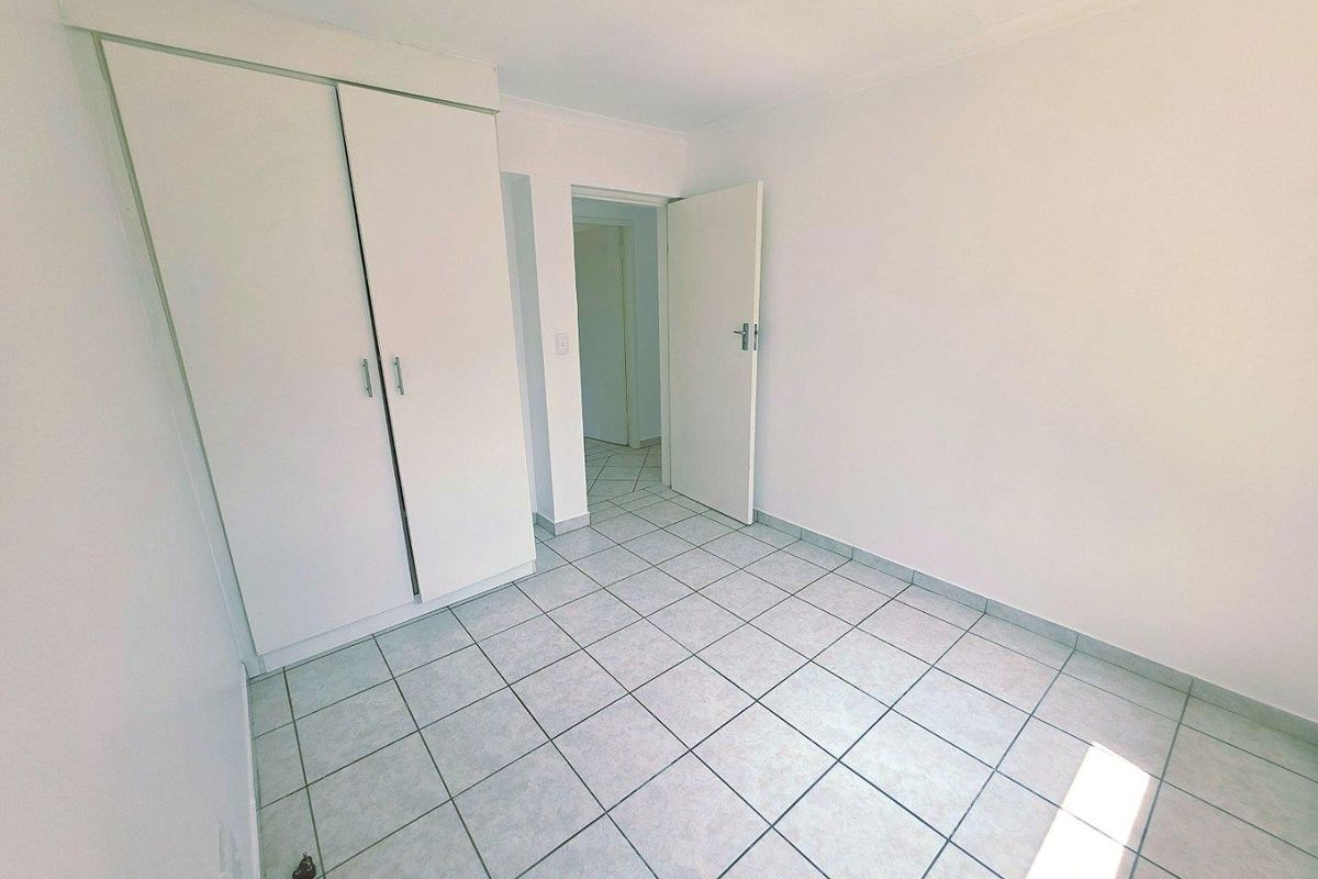 An empty bedroom featuring neutral ceramic floor tiles and a built-in wardrobe, offering a clean, blank canvas for personalization.