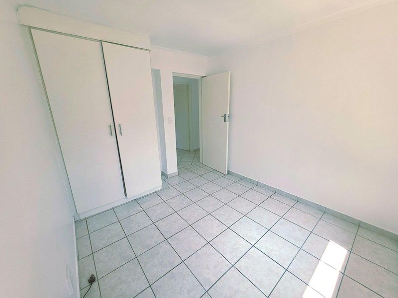 An empty bedroom featuring neutral ceramic floor tiles and a built-in wardrobe, offering a clean, blank canvas for personalization.