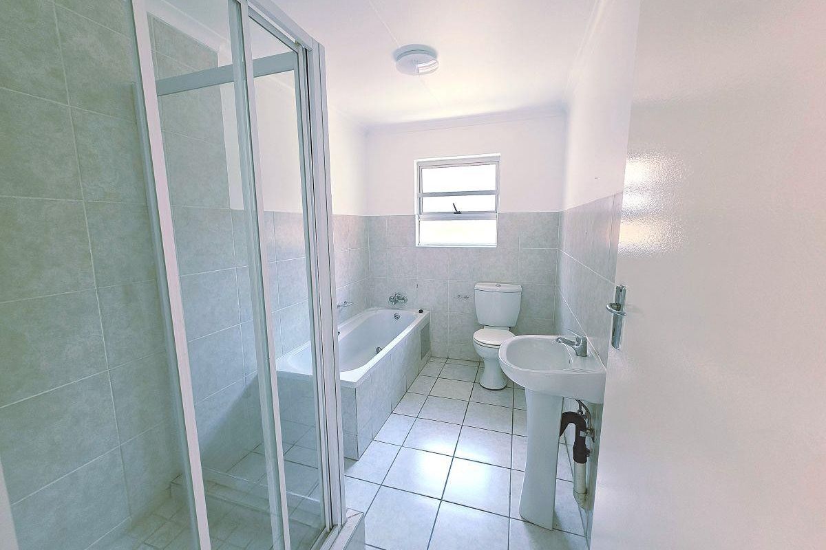 A clean, functional bathroom featuring a separate shower enclosure, bathtub, pedestal basin, and toilet with neutral tiled finishes throughout.