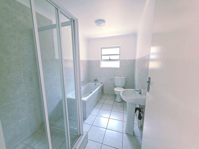A clean, functional bathroom featuring a separate shower enclosure, bathtub, pedestal basin, and toilet with neutral tiled finishes throughout.