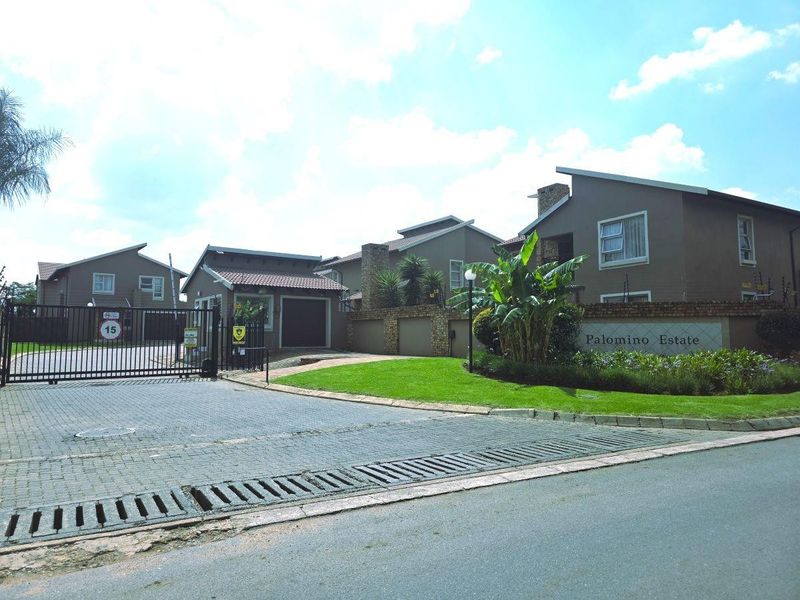 The entrance to Palomino Estate featuring a secure gated access point, paved driveway, and well-maintained landscaped garden areas.