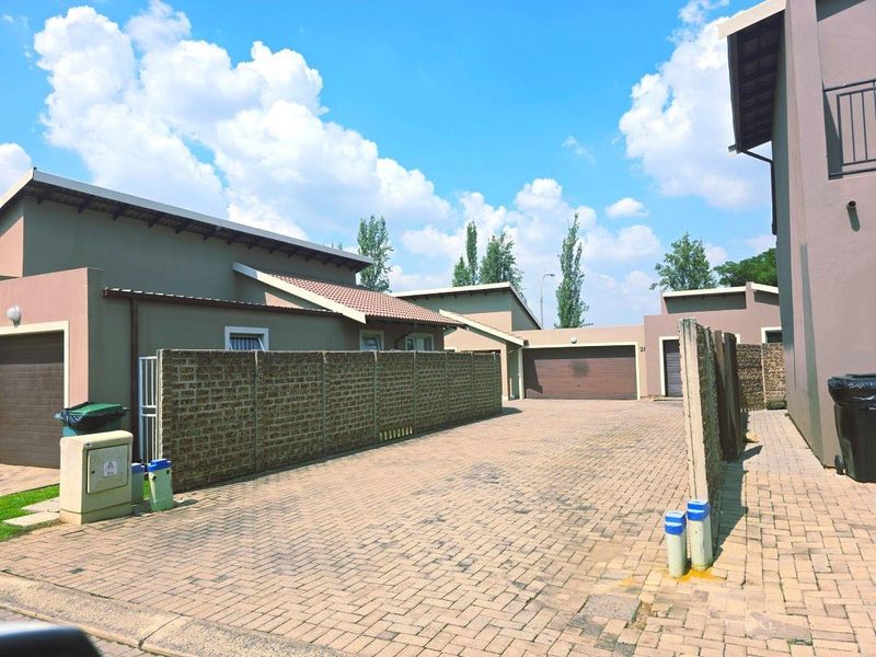 Exterior view of a townhouse complex featuring a paved driveway, brick boundary walls, and multiple garage access points.
