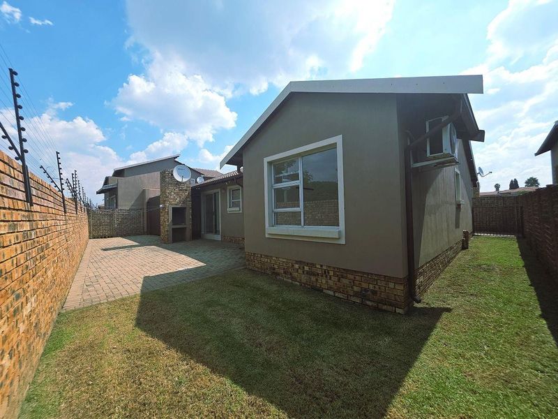 Rear view of the townhouse featuring a paved patio with a built-in braai, a private lawn, and secure brick boundary walls with electric fencing.