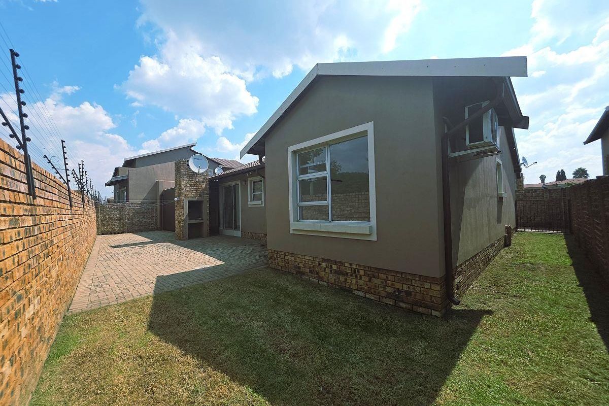 Rear view of the townhouse featuring a paved patio with a built-in braai, a private lawn, and secure brick boundary walls with electric fencing.