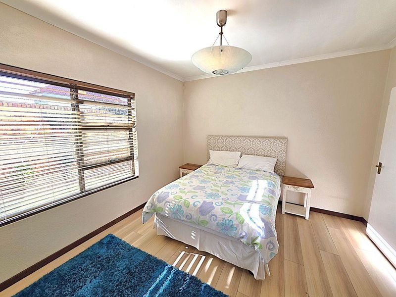 A well-maintained bedroom featuring light-toned laminate flooring, neutral wall finishes, and large windows fitted with venetian blinds for natural light control.