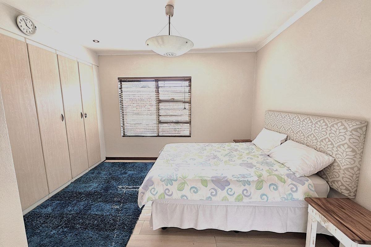 A well-lit bedroom featuring built-in wooden cupboards, neutral wall finishes, and venetian blinds, providing a functional and comfortable sleeping space.