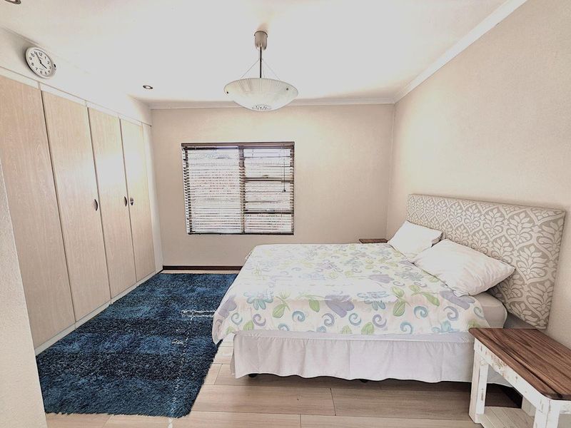 A well-lit bedroom featuring built-in wooden cupboards, neutral wall finishes, and venetian blinds, providing a functional and comfortable sleeping space.