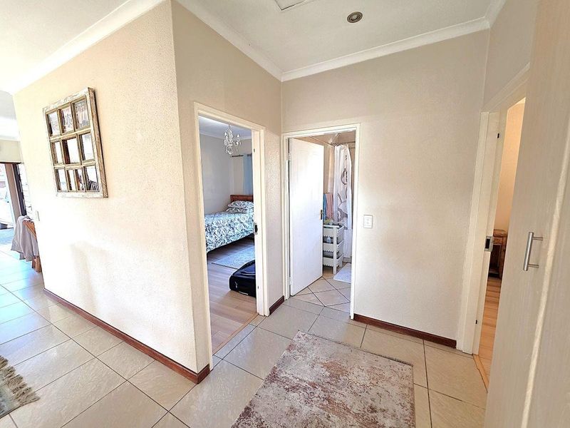 A bright and neutral hallway featuring tiled flooring, recessed lighting, and access to multiple bedrooms and bathrooms.