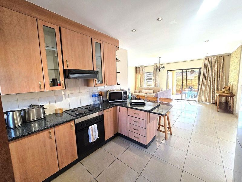 Open-plan kitchen and living area featuring wood-finish cabinetry, granite countertops, built-in appliances, and tiled flooring leading to a patio through sliding glass doors.