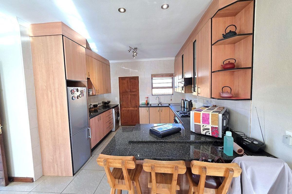 Functional kitchen featuring granite countertops, ample laminate cabinetry, built-in cooking appliances, and tiled flooring with a breakfast bar area.