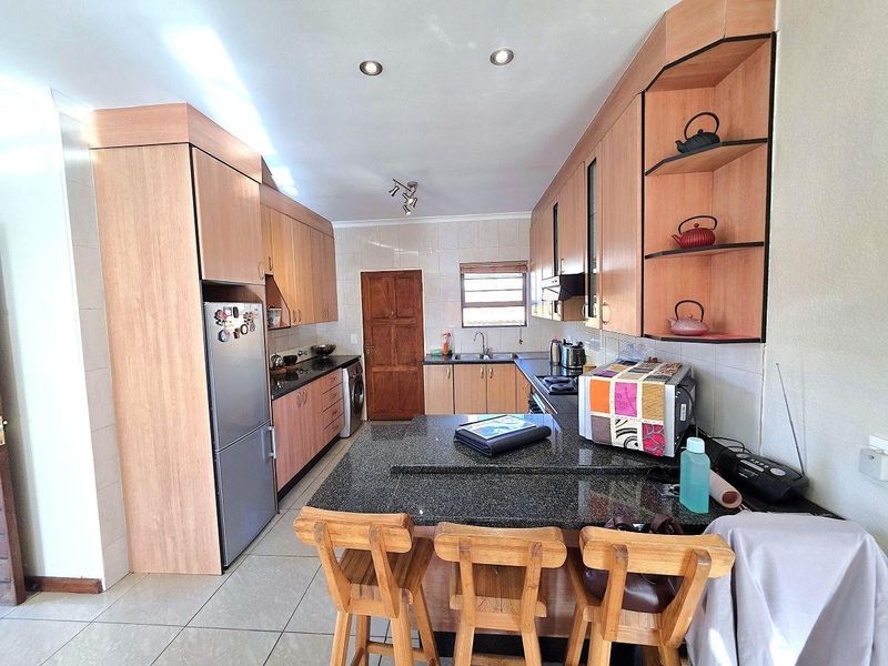 Functional kitchen featuring granite countertops, ample laminate cabinetry, built-in cooking appliances, and tiled flooring with a breakfast bar area.