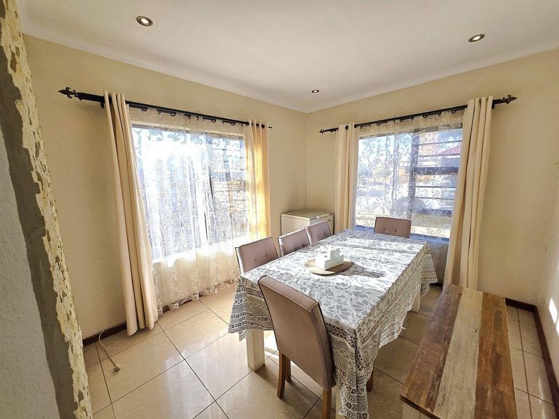 A dining room featuring tiled flooring and recessed downlights, with dual windows providing natural light.