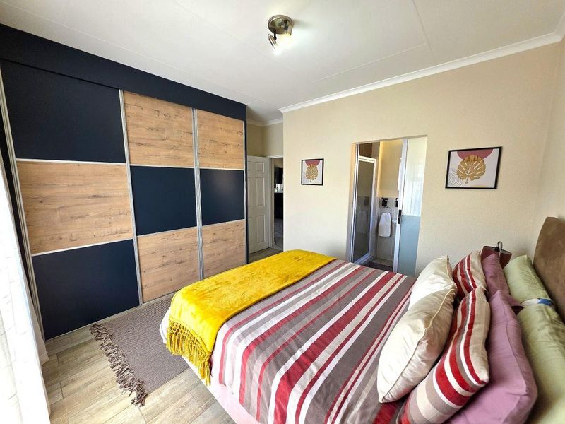 A well-maintained bedroom featuring modern built-in wardrobes with wood-grain and dark blue panels, tiled flooring, and direct access to an en-suite bathroom.
