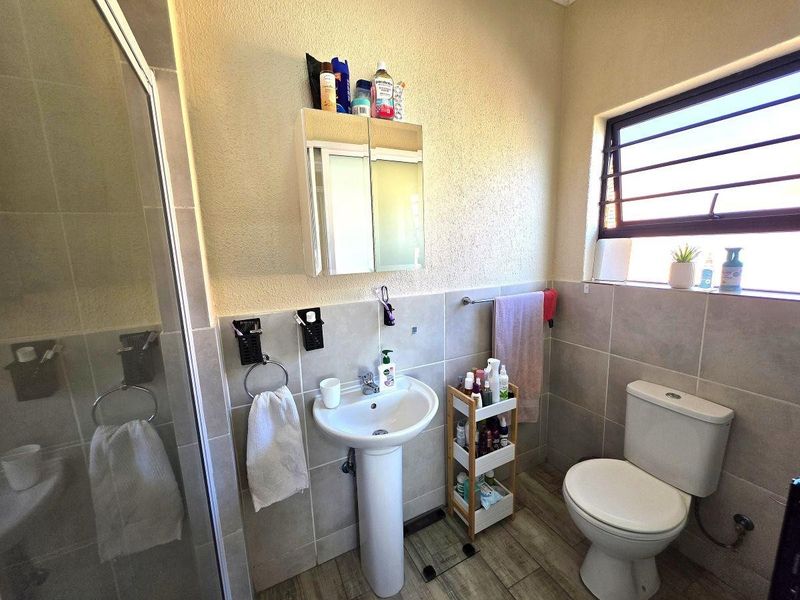 A functional bathroom featuring a pedestal basin, toilet, and shower enclosure with tiled finishes and a louvered window for natural ventilation.