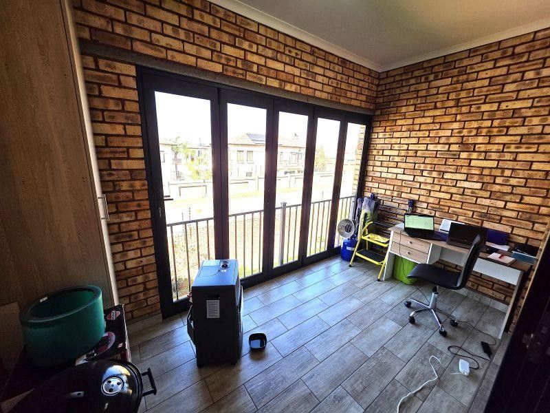A bright office space featuring exposed brick walls, modern tiled flooring, and large black aluminium folding doors leading to a balcony.