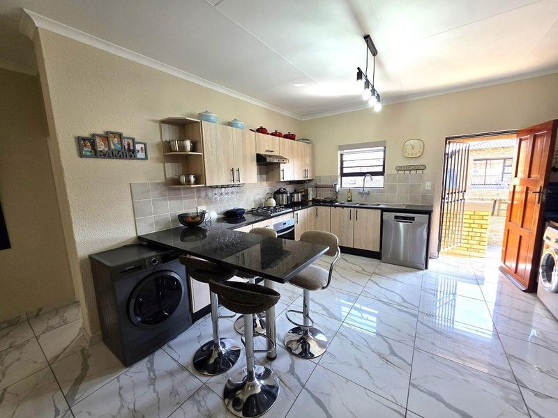 Modern kitchen featuring light wood cabinetry, granite countertops, integrated appliances, and tiled flooring with direct access to an outdoor area.