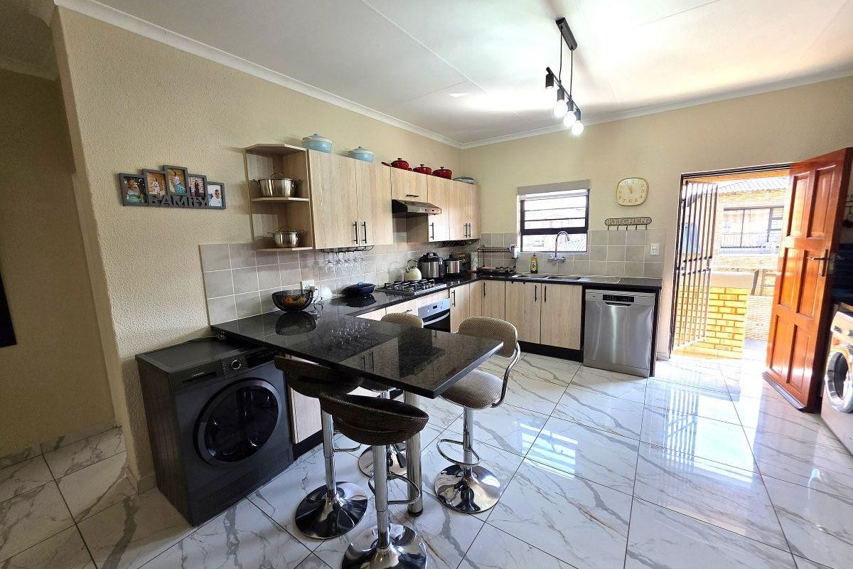 Modern kitchen featuring light wood cabinetry, granite countertops, integrated appliances, and tiled flooring with direct access to an outdoor area.