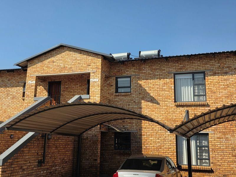 Front elevation of a face brick apartment building featuring a covered carport, solar water heating system, and secure entrance access.