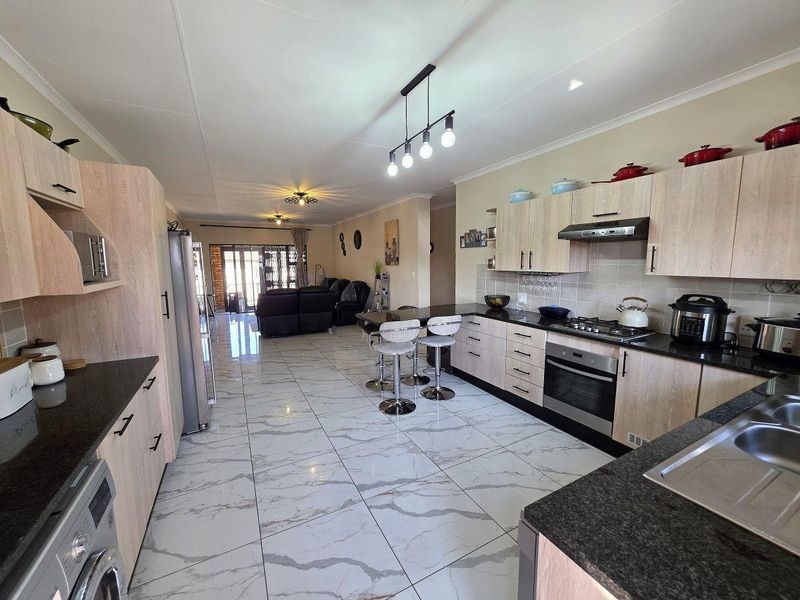 Spacious open-plan kitchen and living area featuring modern light wood cabinetry, granite countertops, high-gloss marble-look floor tiles, and integrated cooking appliances.
