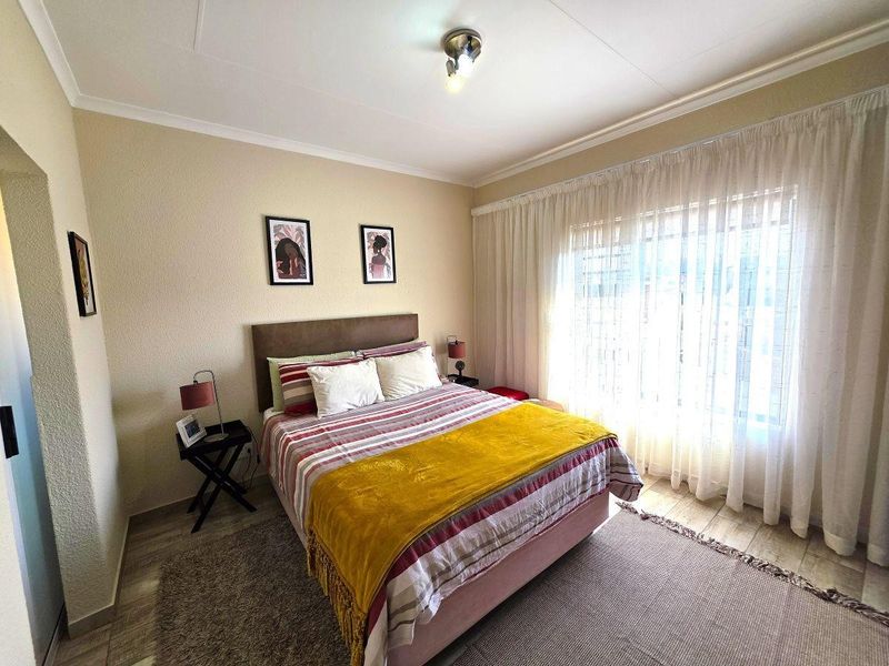 A well-lit bedroom featuring tiled flooring, textured walls, and large windows with curtain tracks, providing a functional and comfortable living space.