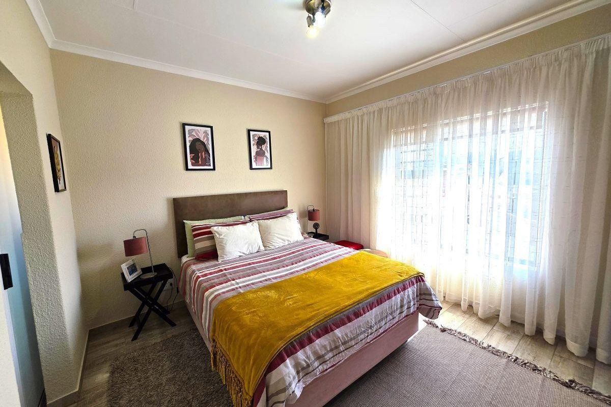 A well-lit bedroom featuring tiled flooring, textured walls, and large windows with curtain tracks, providing a functional and comfortable living space.