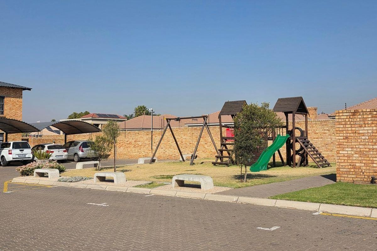 Communal outdoor area featuring a playground, paved parking bays with carports, and secure brick boundary walls within the apartment complex.