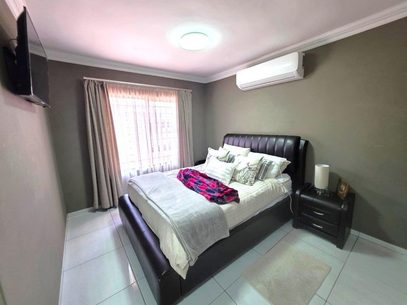 A well-maintained bedroom featuring tiled flooring, a wall-mounted air conditioning unit, and neutral wall tones, providing a comfortable and functional living space.