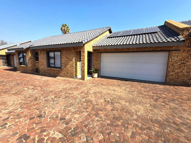 Front view of a face brick house featuring a tiled roof, solar panels, and a double garage, set against a paved cobblestone driveway.