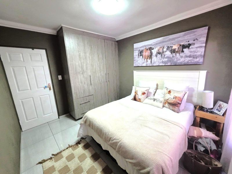 A well-maintained bedroom featuring neutral tiled flooring, built-in wooden cupboards, and decorative ceiling cornicing.