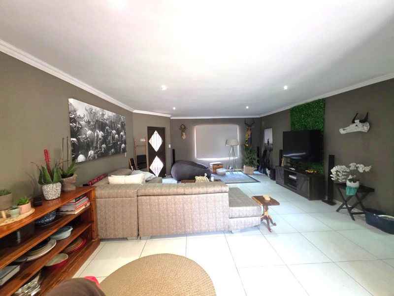 Spacious living room featuring neutral tiled flooring, recessed downlighting, and a decorative entrance door, offering a comfortable and well-maintained living space.