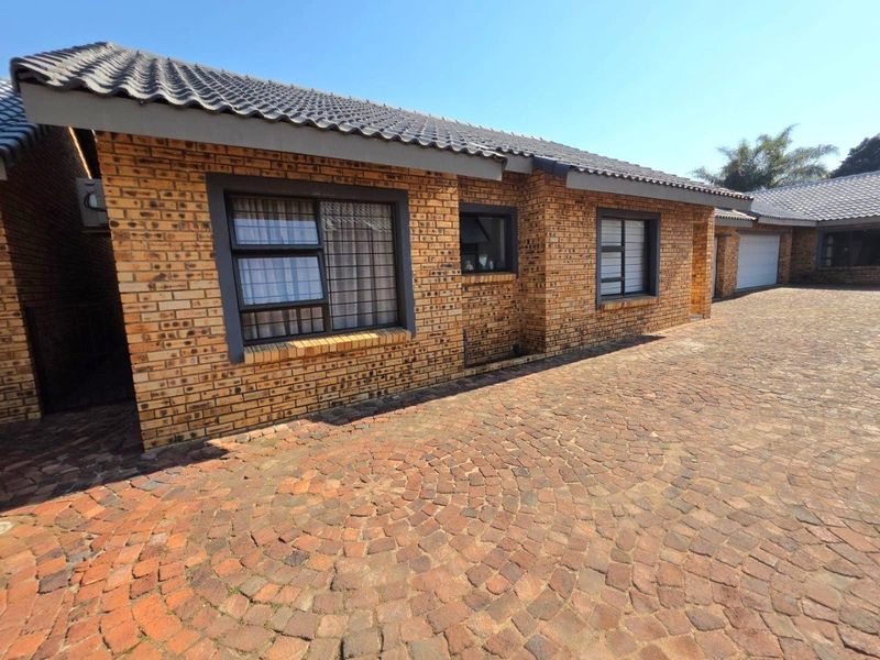 A well-maintained face brick house exterior featuring a paved driveway, tiled roof, and secure aluminium-framed windows.
