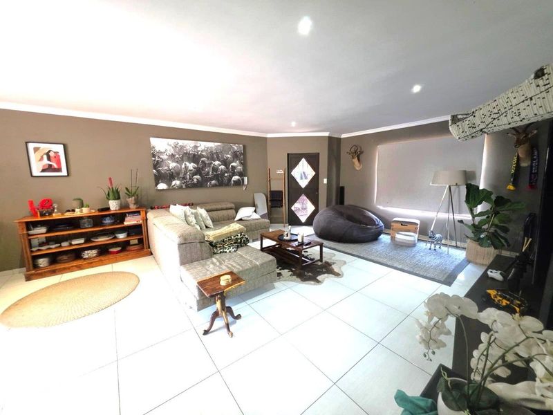 Spacious living room featuring neutral tiled flooring, recessed downlighting, and a decorative timber entrance door, offering a comfortable and well-maintained living space.