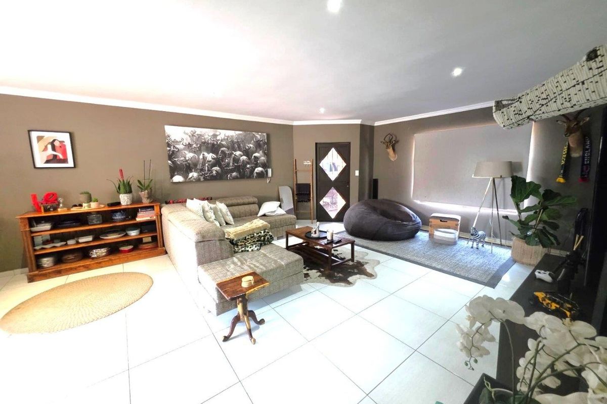 Spacious living room featuring neutral tiled flooring, recessed downlighting, and a decorative timber entrance door, offering a comfortable and well-maintained living space.