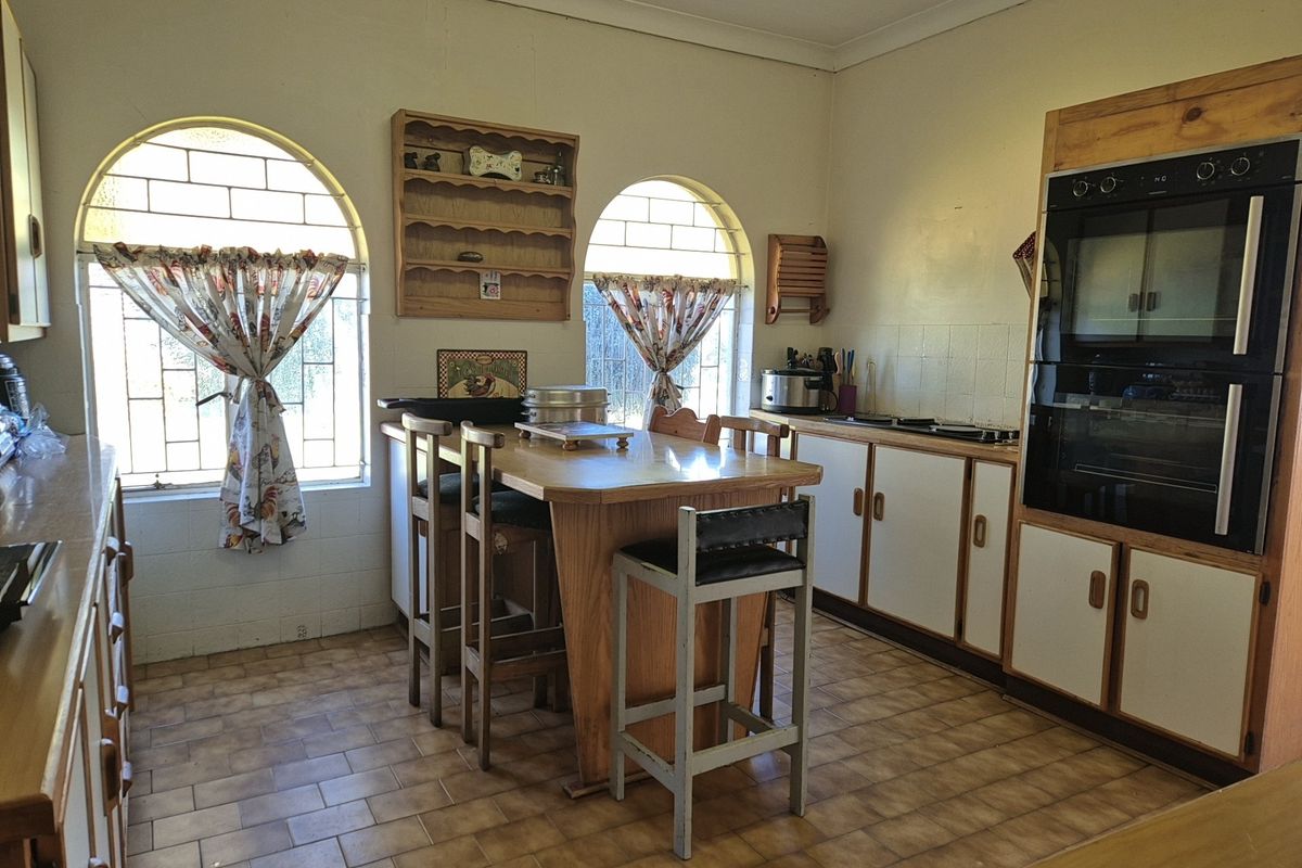 A dated kitchen featuring built-in double ovens, hob, tiled flooring, and distinctive arched windows with security bars.