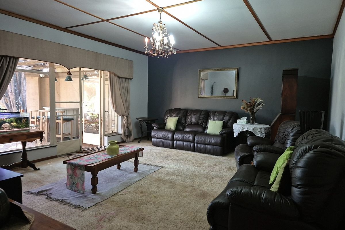 Spacious living room featuring a timber-grid ceiling, chandelier lighting, and large sliding glass doors providing access to an outdoor patio area.