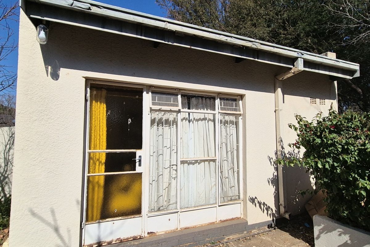 Rear exterior view of the property featuring a metal-framed sliding door with security gate, guttering, and downpipe, showing signs of weathering.
