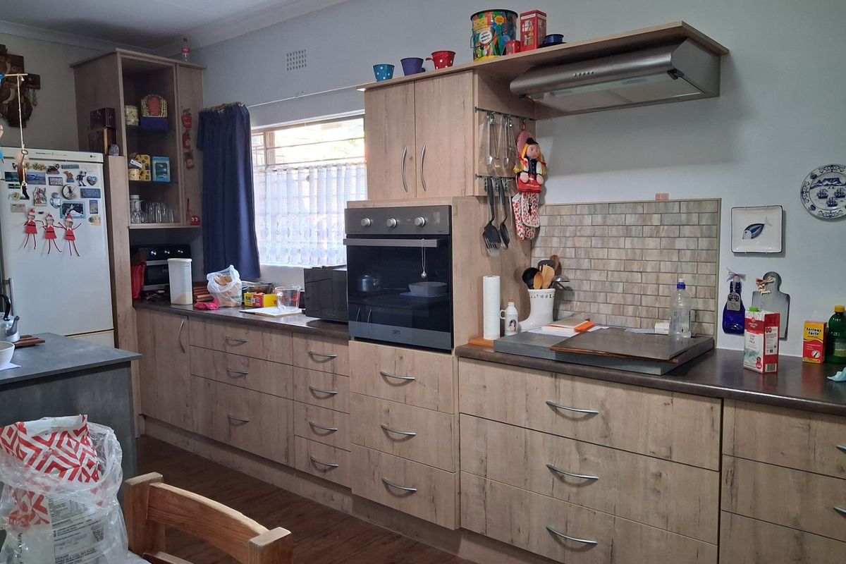 A functional kitchen featuring wood-look cabinetry, built-in oven, extractor fan, and tiled backsplash with ample counter space.