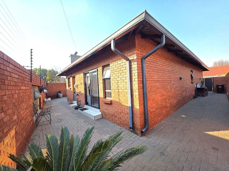 A view of the rear exterior featuring face brick walls, paved courtyard area, sliding door access, and secure boundary wall with electric fencing.