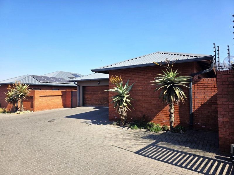 Front exterior view of a modern brick house featuring a paved driveway, garage, and secure electric fencing.