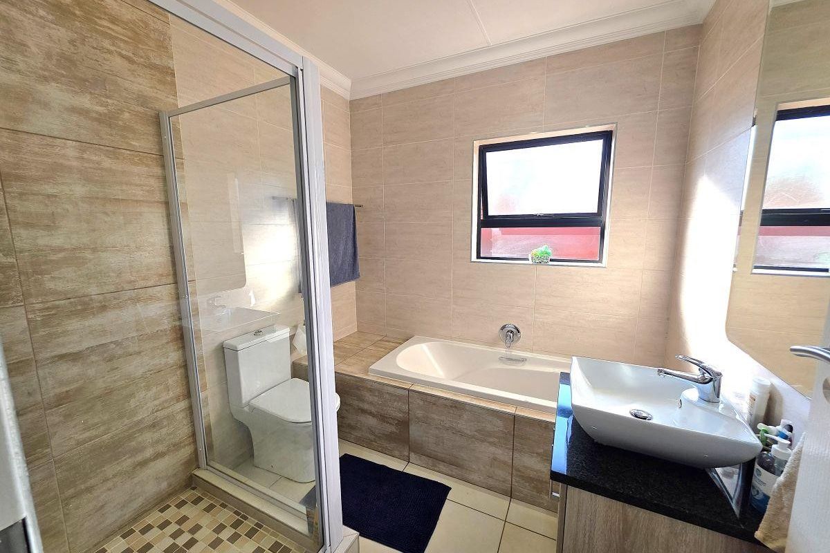 Modern bathroom featuring a glass-enclosed shower, a built-in bathtub, a vessel sink vanity, and neutral floor-to-ceiling tiling.