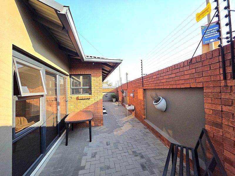 A paved side walkway featuring a brick boundary wall with integrated electric fencing and modern aluminium window and door frames.