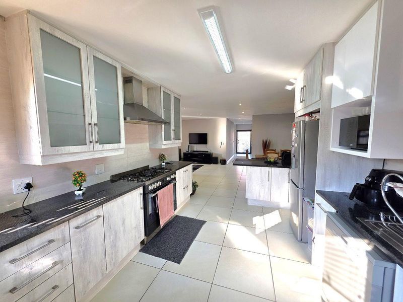 Modern open-plan kitchen featuring light wood-grain cabinetry, granite countertops, gas hob, and integrated appliances, flowing seamlessly into the living and dining areas.