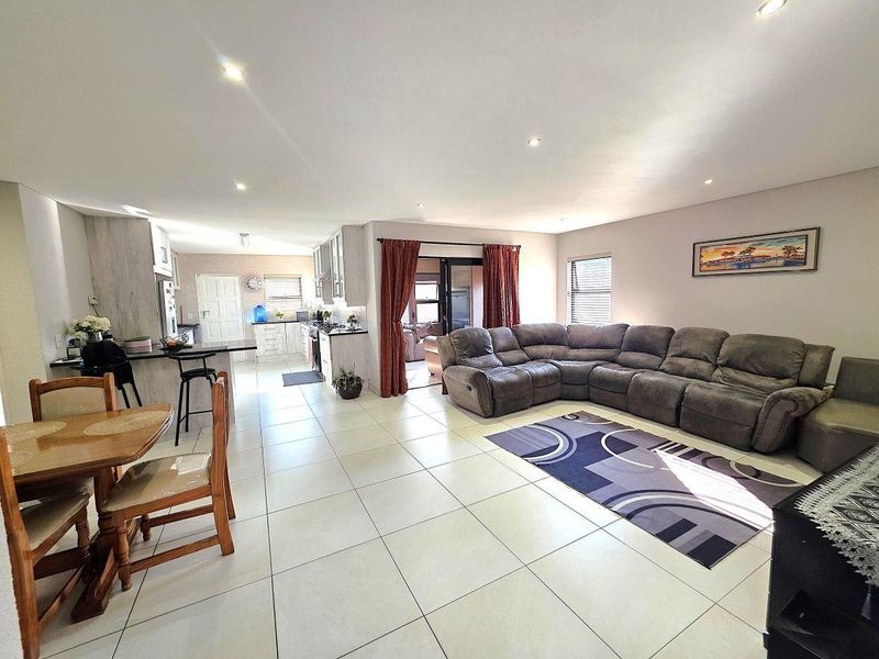 Spacious open-plan living area featuring tiled floors, recessed lighting, and a modern kitchen with an island, seamlessly connecting to the outdoor patio area.