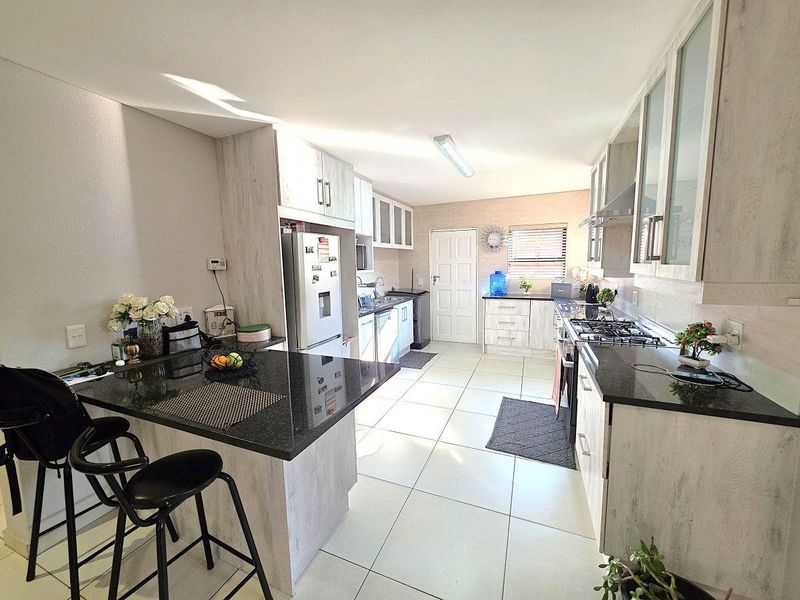 Modern kitchen featuring light wood-grain cabinetry, dark granite countertops, a gas hob, and tiled flooring with an integrated breakfast bar.