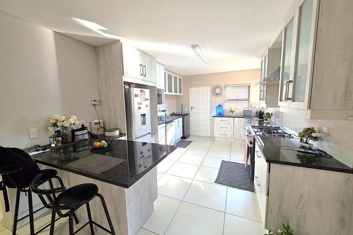 Modern kitchen featuring light wood-grain cabinetry, dark granite countertops, a gas hob, and tiled flooring with an integrated breakfast bar.