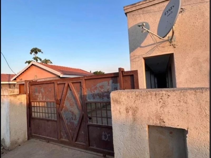 Front exterior view of the property featuring a metal driveway gate, masonry boundary wall, and a mounted satellite dish.