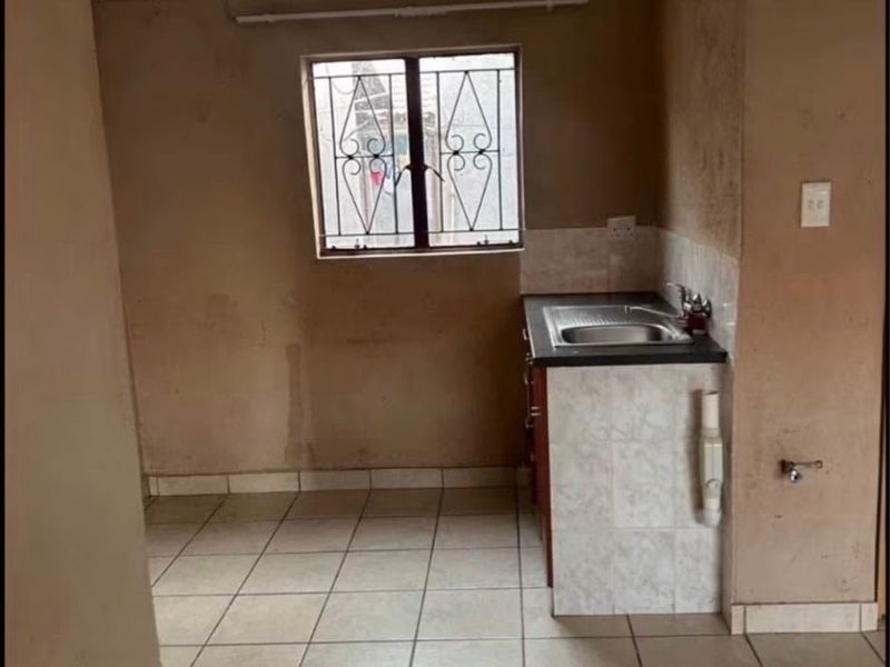 A compact, empty kitchen area featuring tiled flooring, a stainless steel sink, and built-in cabinetry, requiring cosmetic updates to the wall finishes.