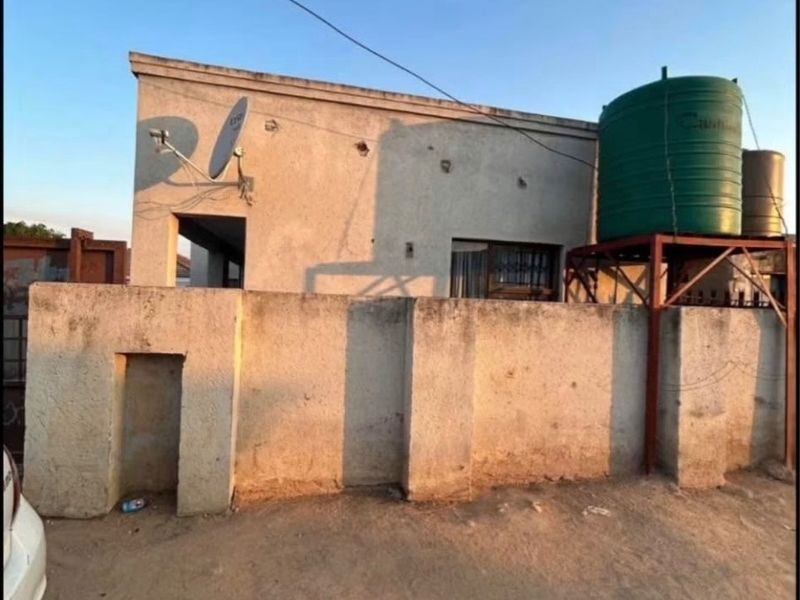 Exterior view of a residential property featuring a boundary wall, water storage tank on a metal stand, and a satellite dish installation.