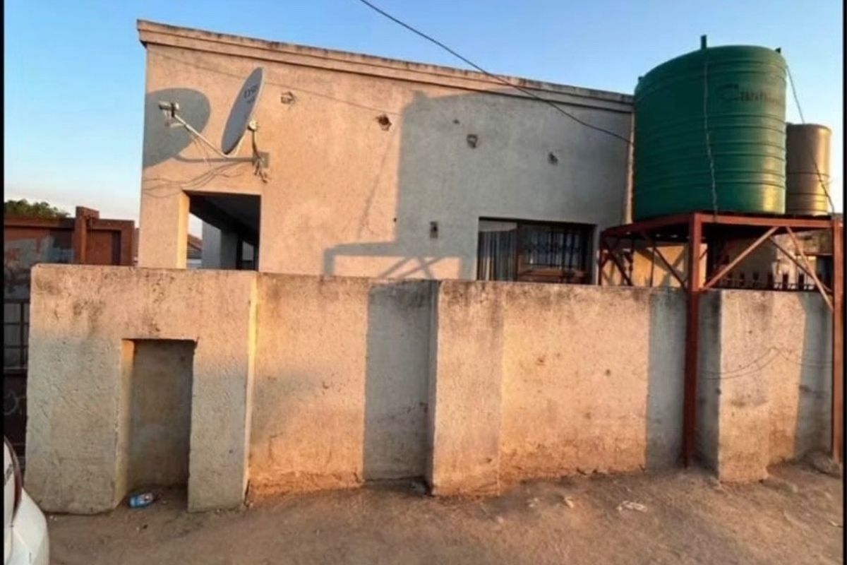 Exterior view of a residential property featuring a boundary wall, water storage tank on a metal stand, and a satellite dish installation.