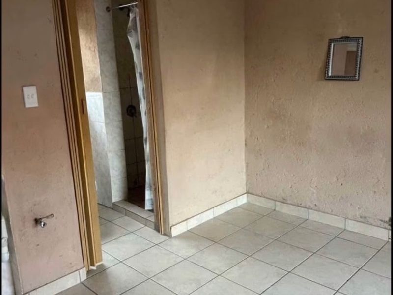 An empty bedroom featuring tiled flooring and direct access to an en-suite bathroom with a shower.